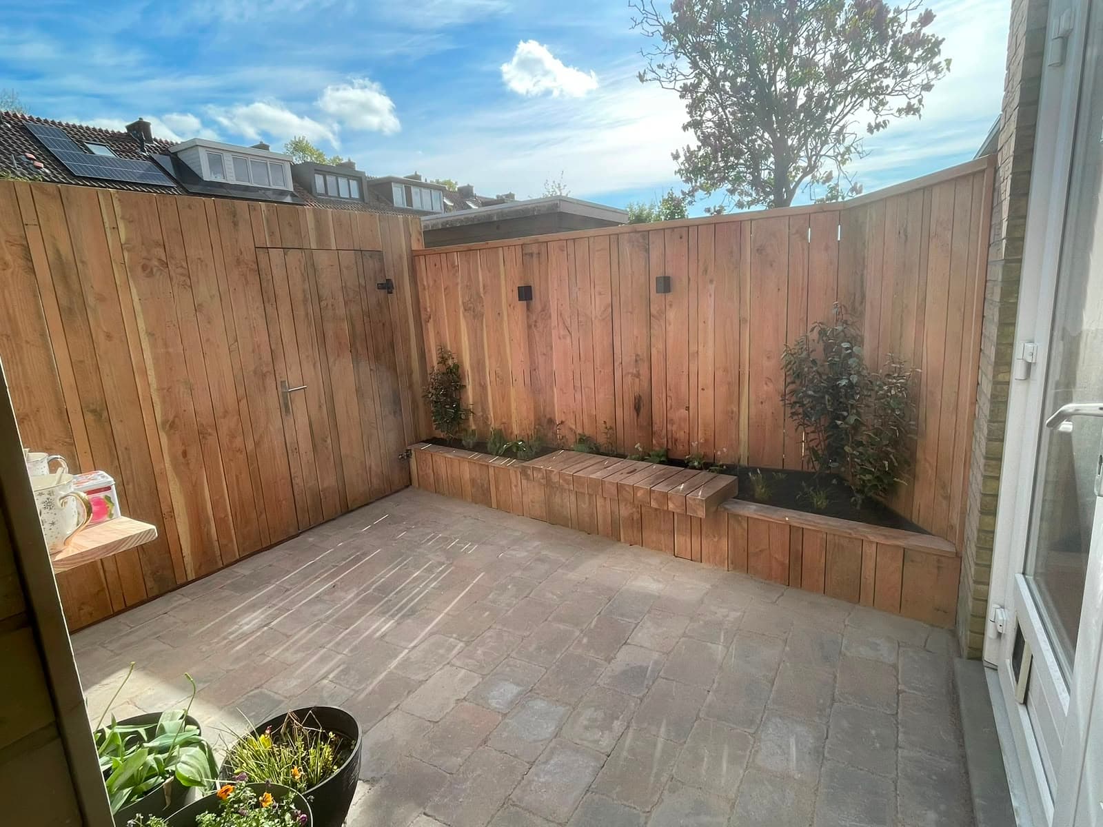 Horizontale houten schutting met ingebouwde zitbank op een terras met klinkerbestrating